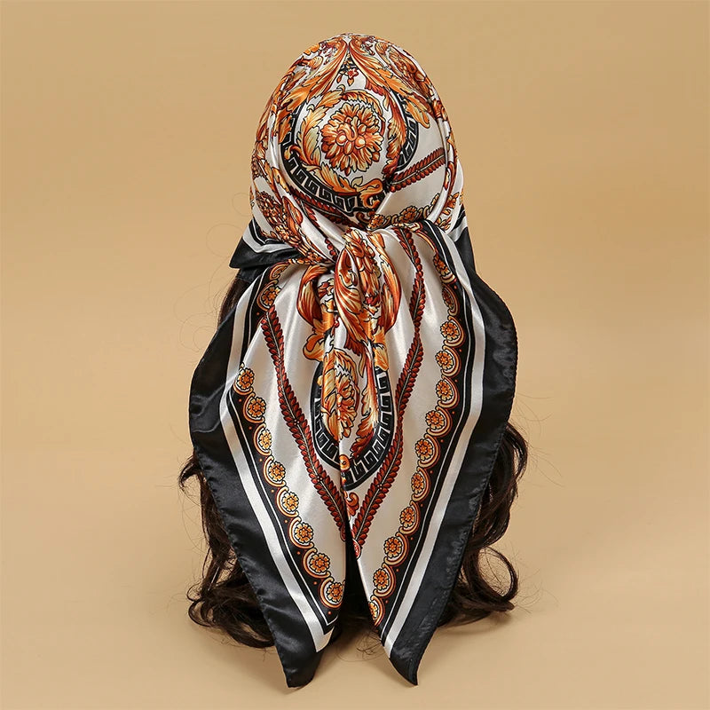 An elegant satin square scarf featuring intricate floral patterns in orange, gold, and white on a black background.