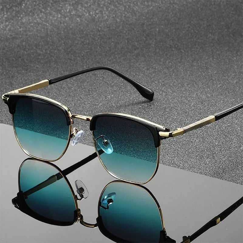 Vintage square metal frame sunglasses with gold accents and teal lenses resting on a reflective surface.