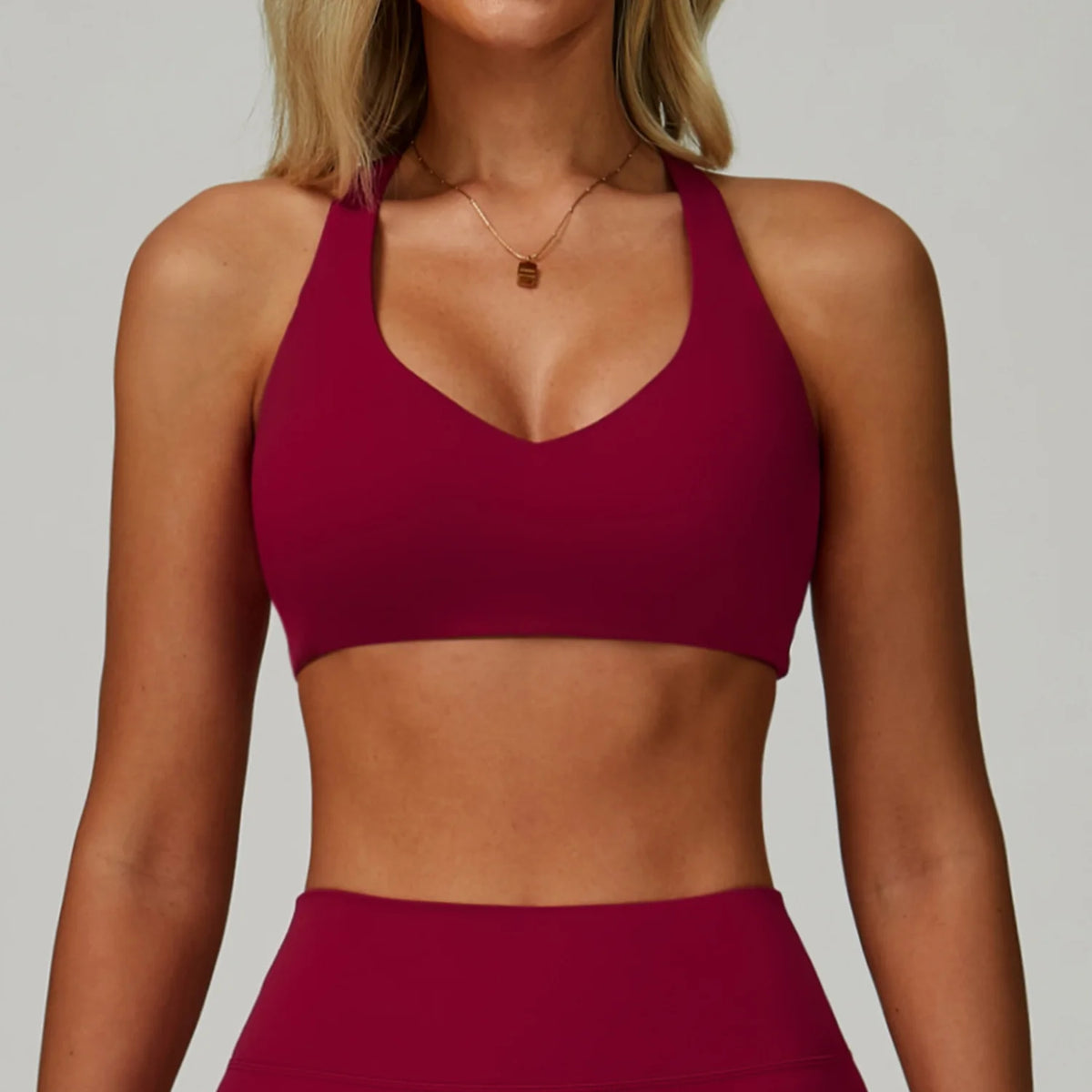 A model wearing a maroon padded sport yoga bra and matching bottoms, featuring a V-neck design.