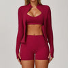 A woman wearing a maroon 3-piece yoga sports set consisting of a long-sleeved cropped top and matching shorts.