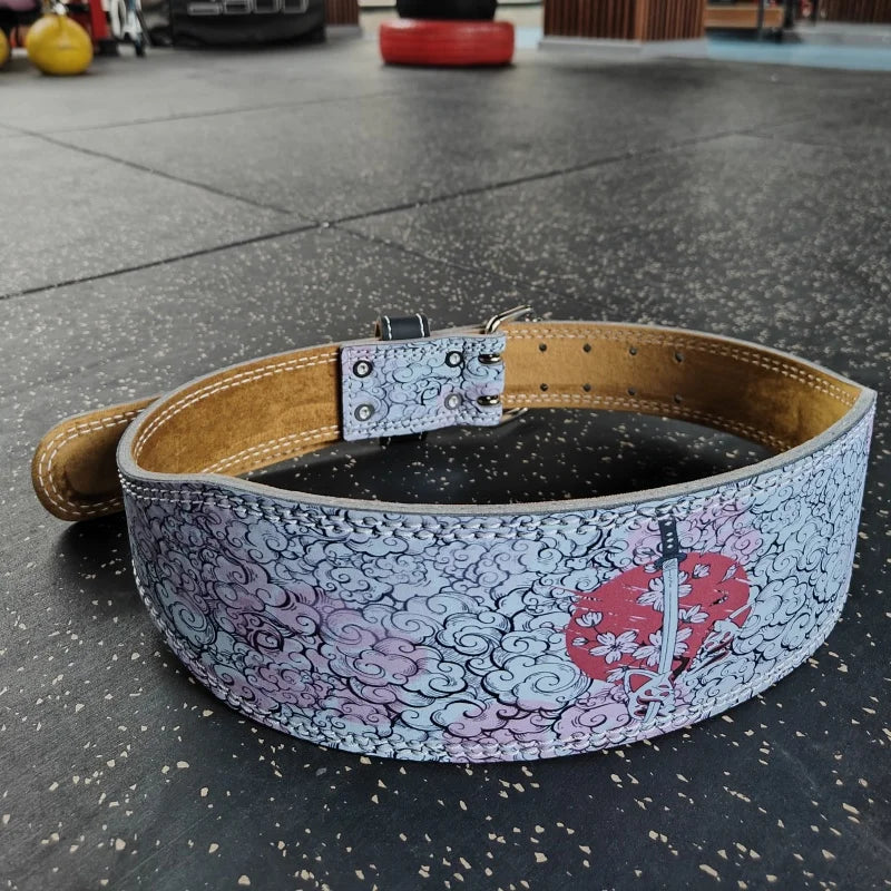 A beige weightlifting belt with a patterned design featuring pink and black swirling motifs and a silver buckle.
