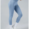 A person wearing light blue high-waist yoga leggings and white socks standing against a light gray background.