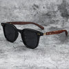 Black sunglasses with dark lenses and a brown wood grain frame resting on a gray textured surface.