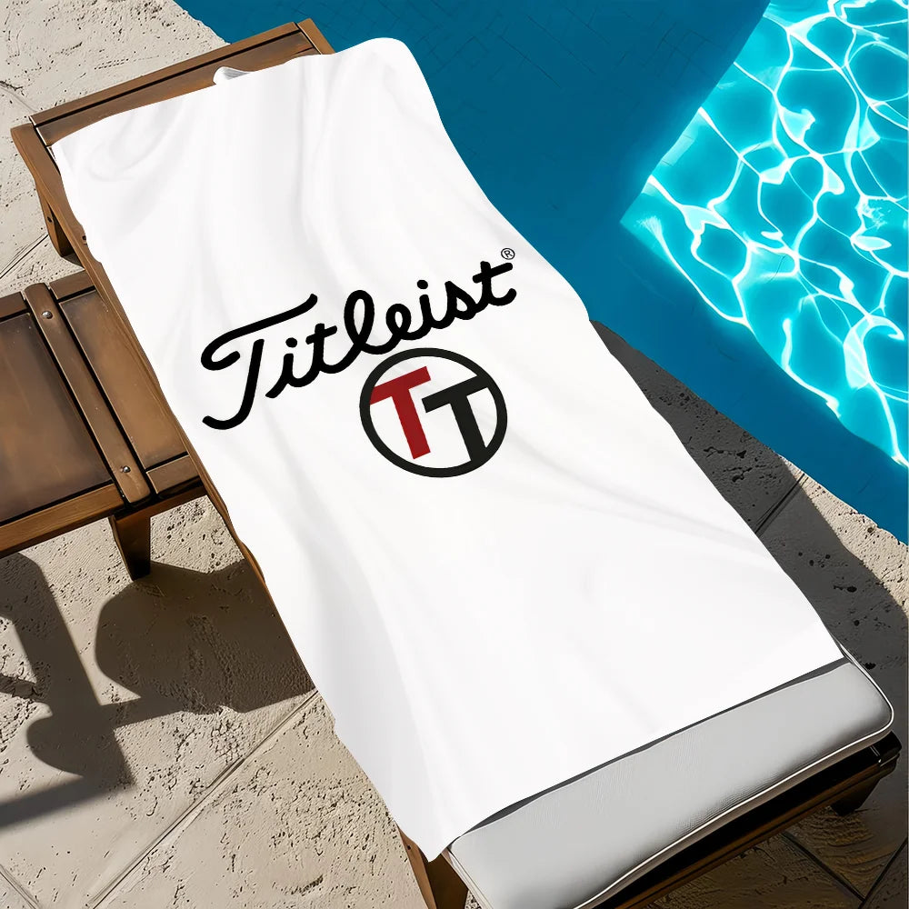 A white Titleist branded beach towel is laid out next to a bright blue swimming pool.
