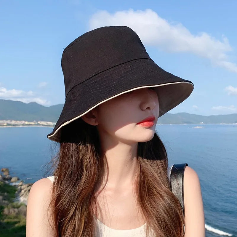 A woman wearing a wide brim bucket hat outdoors against a blue sky and sea background.