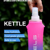 A hand holds a pink and blue silicone sports water bottle with a white cap against a blurred green background.