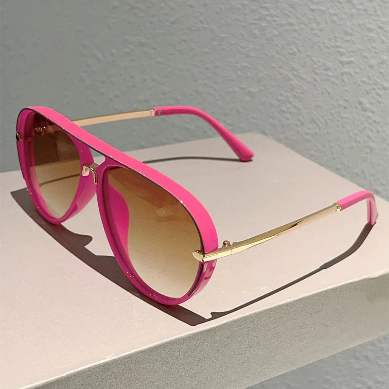 Pink gradient sunglasses with gold accents resting on a light surface.