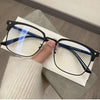 A pair of black retro square blue light blocking eyeglasses resting on a white card next to a person's hand.