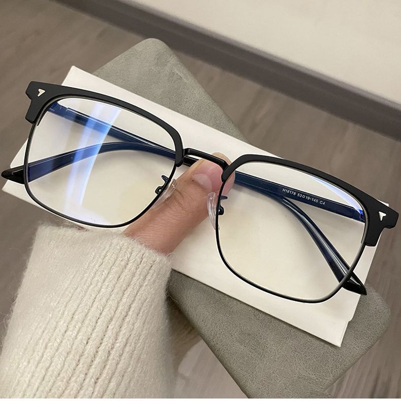 A pair of black retro square blue light blocking eyeglasses resting on a white card next to a person's hand.