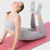 A woman wearing gray athletic wear is performing a stretch on a pink mat, demonstrating Grip Pilates Socks for Yoga and Barre