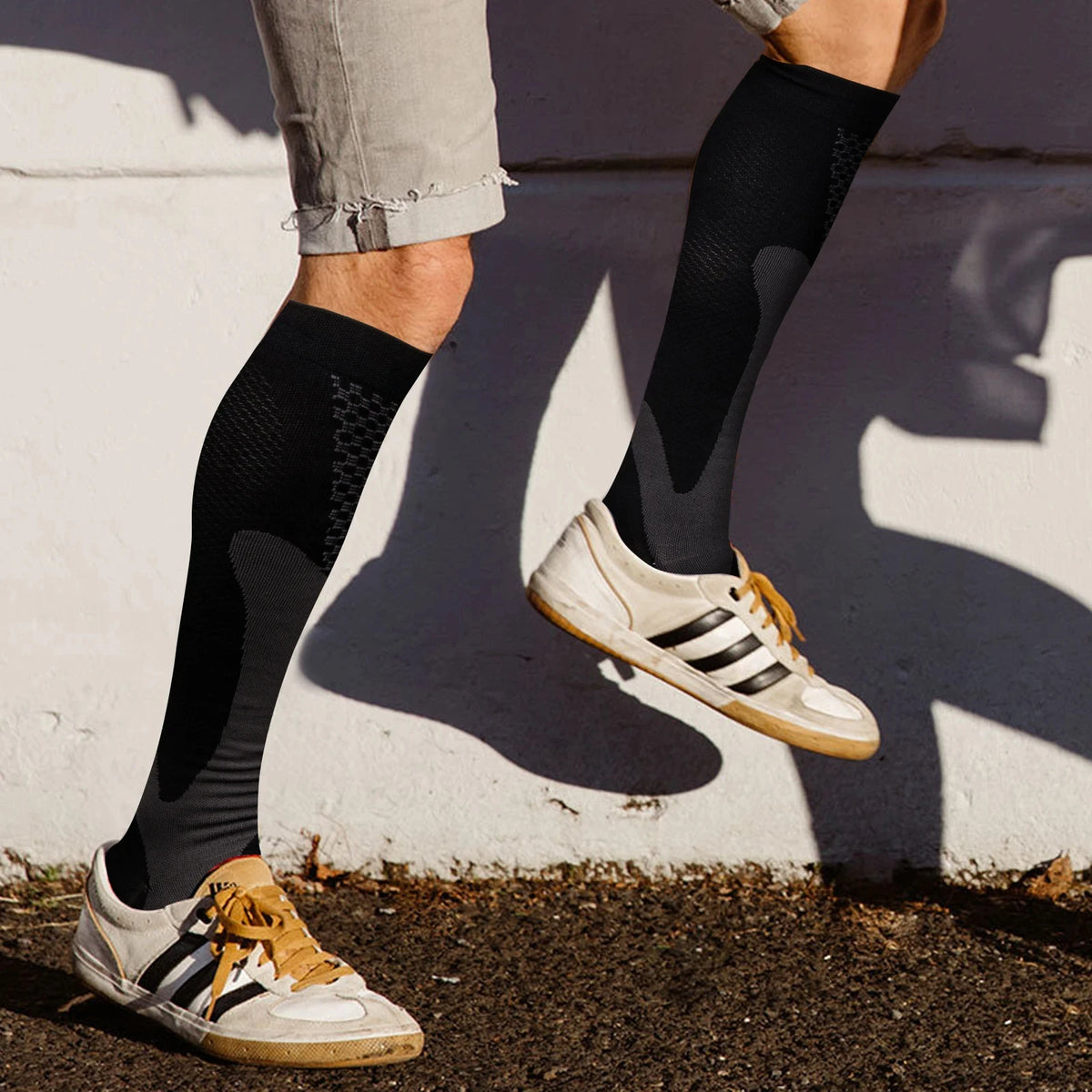 A person wearing black compression socks and white sneakers standing outdoors.