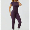Eine Frau modelliert ein Zweiteiler-Yoga-Set mit lila, hoch geschnittener Leggings und einem kurzen Oberteil.