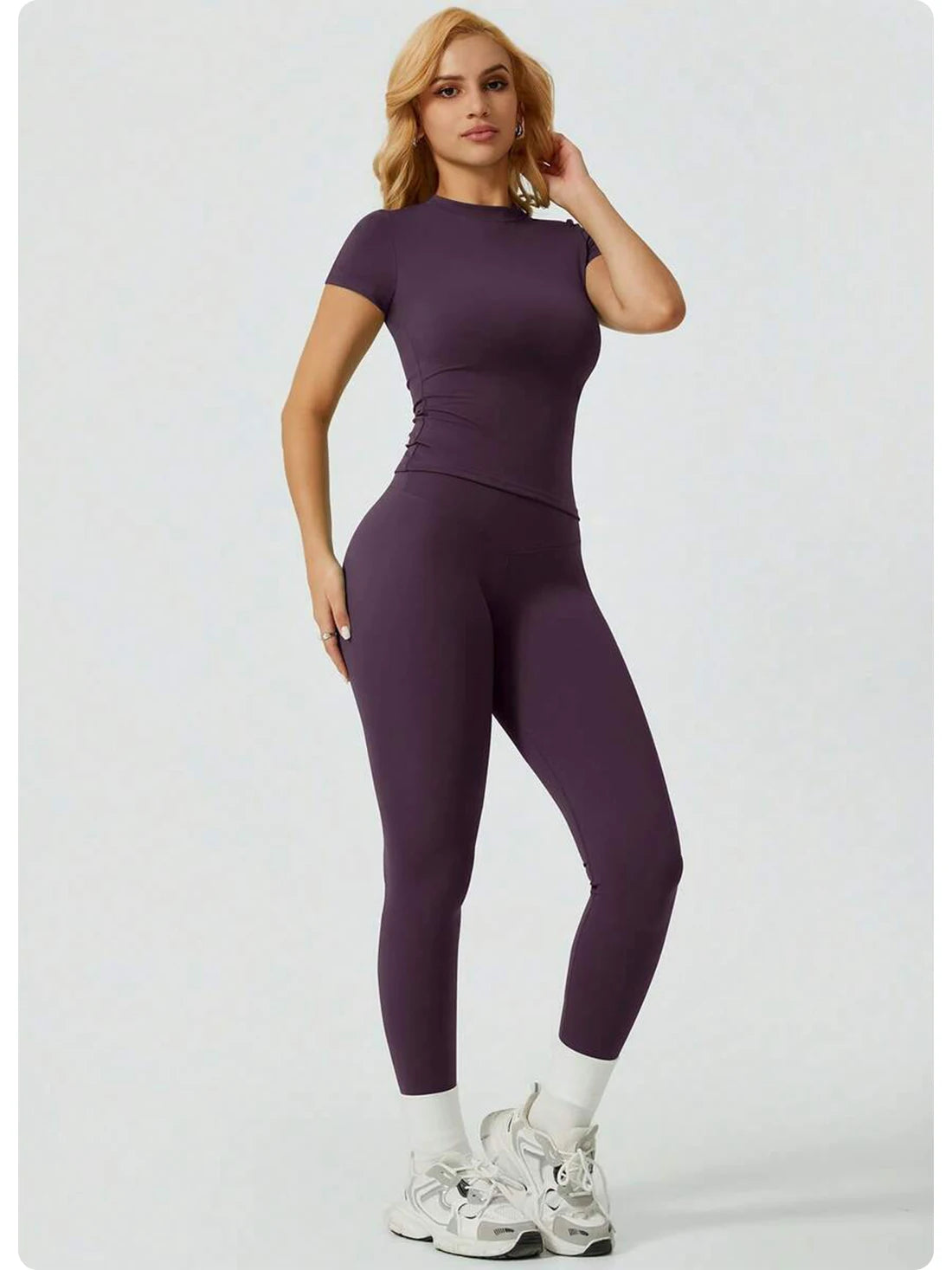 Eine Frau modelliert ein Zweiteiler-Yoga-Set mit lila, hoch geschnittener Leggings und einem kurzen Oberteil.