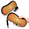 A hand holds an orange and black spider web patterned eyeglass pouch.
