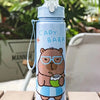 A light blue cartoon drinking water bottle featuring a bear wearing glasses and holding a cup, set against a blurred green ba