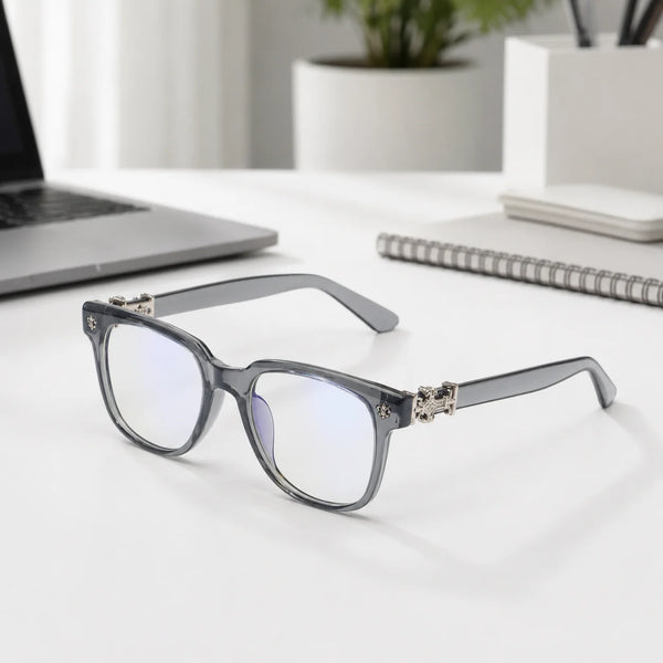 Gray-framed classic square anti-blue light sunglasses resting on a white desk next to a laptop and notebook.