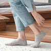 A person wearing gray comfort fit ankle socks while standing on a wooden floor.