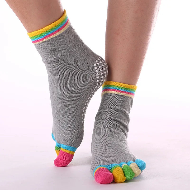 Gray yoga socks with rainbow trim and colorful toe grips worn on a person's foot.