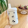 Un tumbler isotherme blanc avec des motifs floraux noirs est tenu sur une table en bois à côté d'un panier de plantes séchées