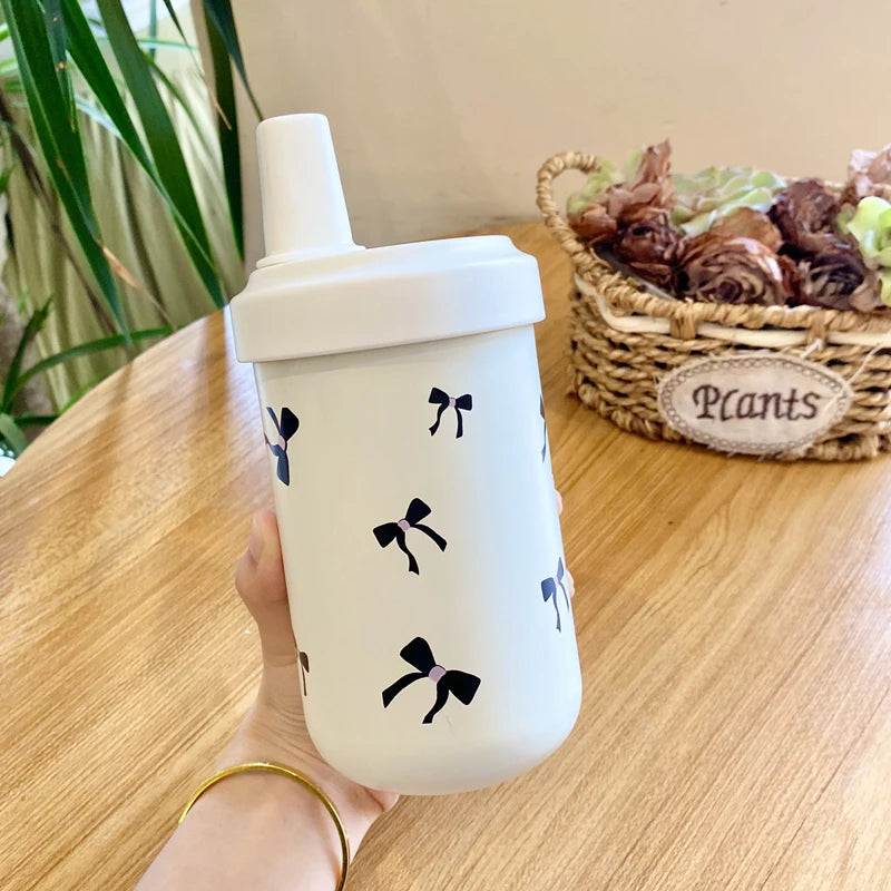 Un tumbler isotherme blanc avec des motifs floraux noirs est tenu sur une table en bois à côté d'un panier de plantes séchées