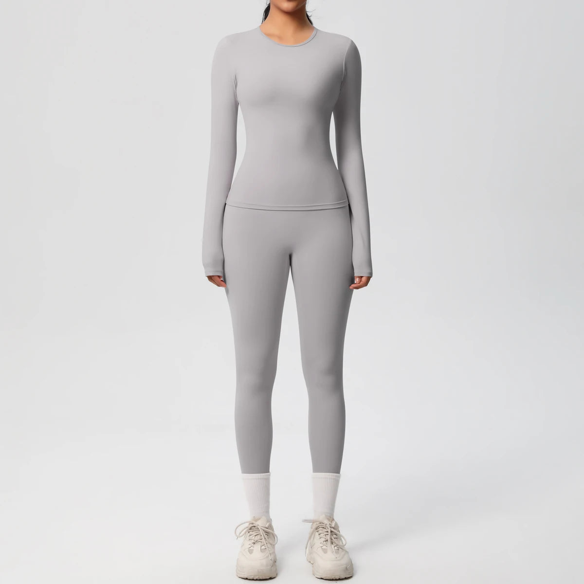 A woman wearing a full-length, long-sleeved grey performance yoga and gym set with matching leggings and white socks.