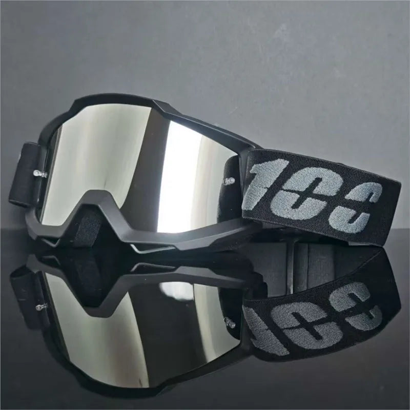 Un par de gafas universales para motocross negras con lentes reflectantes sobre una superficie oscura.