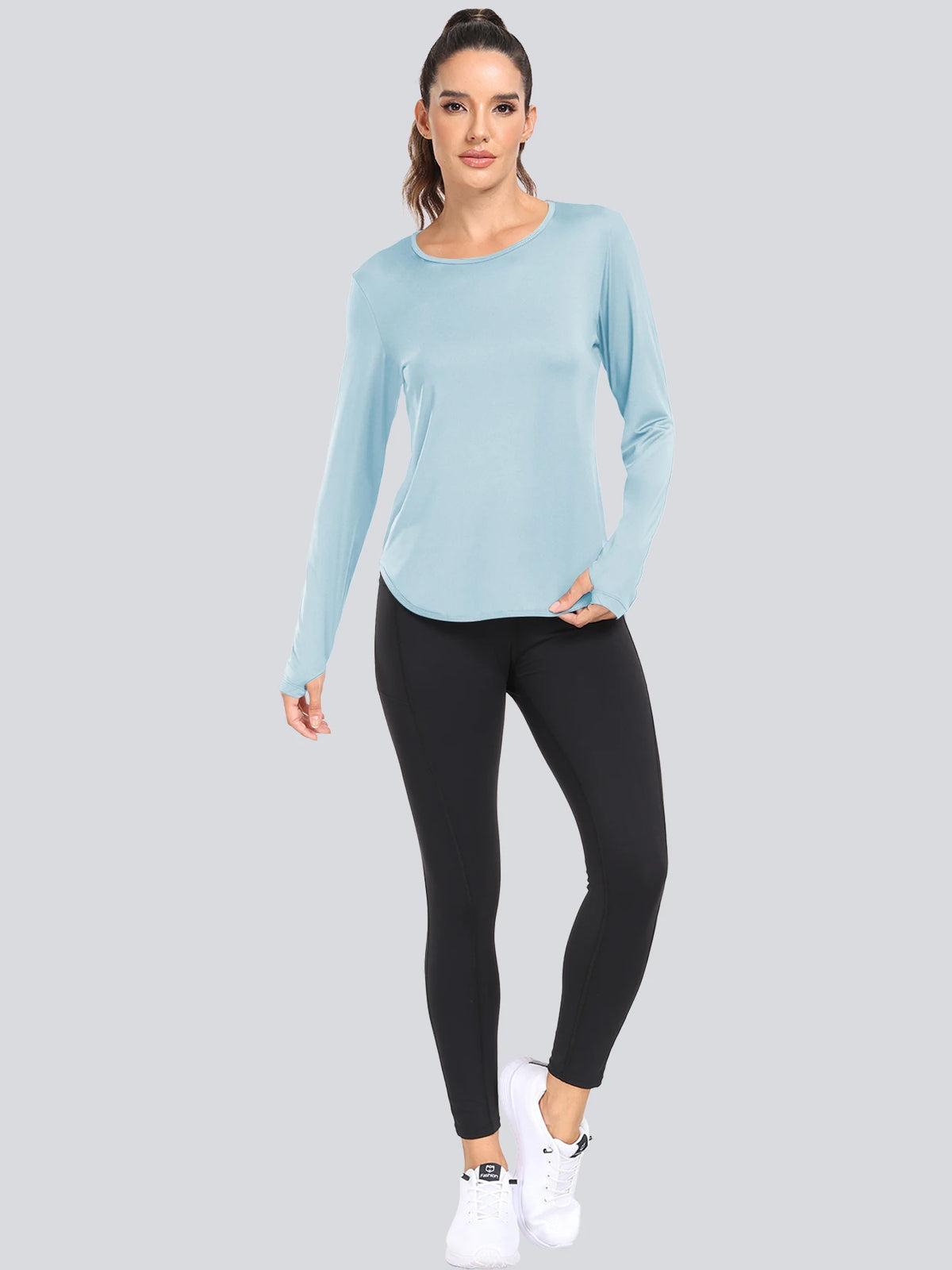 A woman models a light blue long-sleeved loose fit sun protection t-shirt and black leggings.