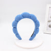 A light blue sponge terry cloth headband for hair styling displayed on a white stand.