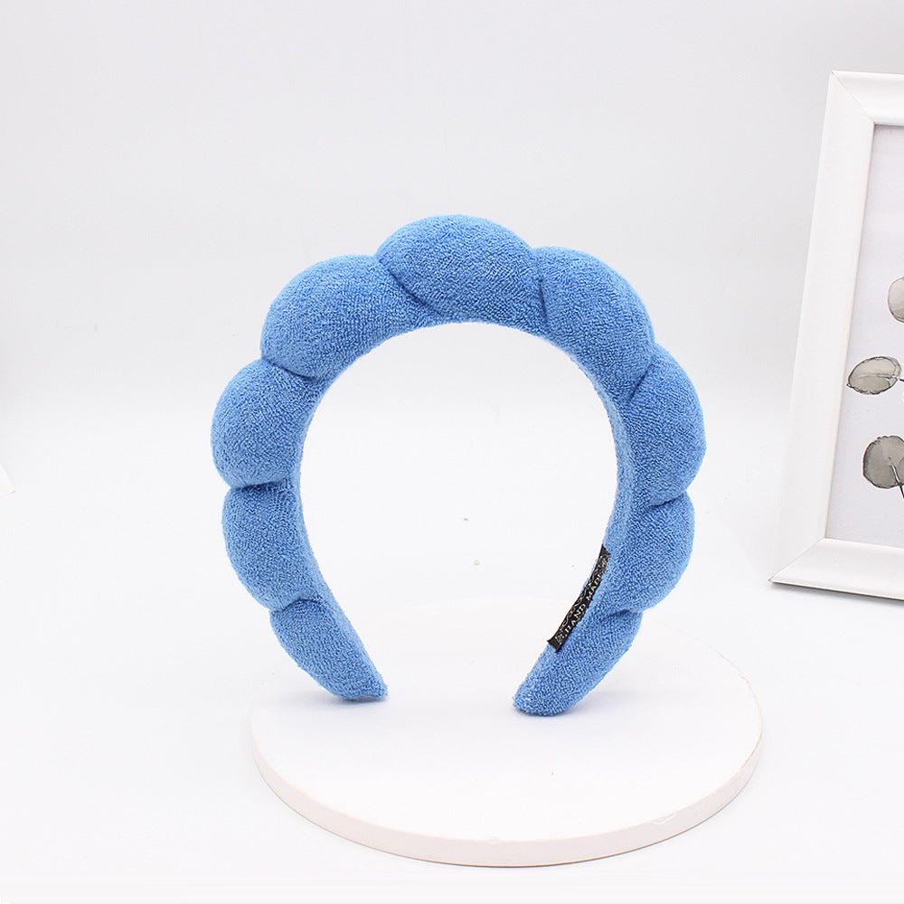 A light blue sponge terry cloth headband for hair styling displayed on a white stand.