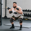Muskulöser Mann macht Kniebeugen mit Kompressionshosen und hebt Hanteln im Fitnessstudio.
