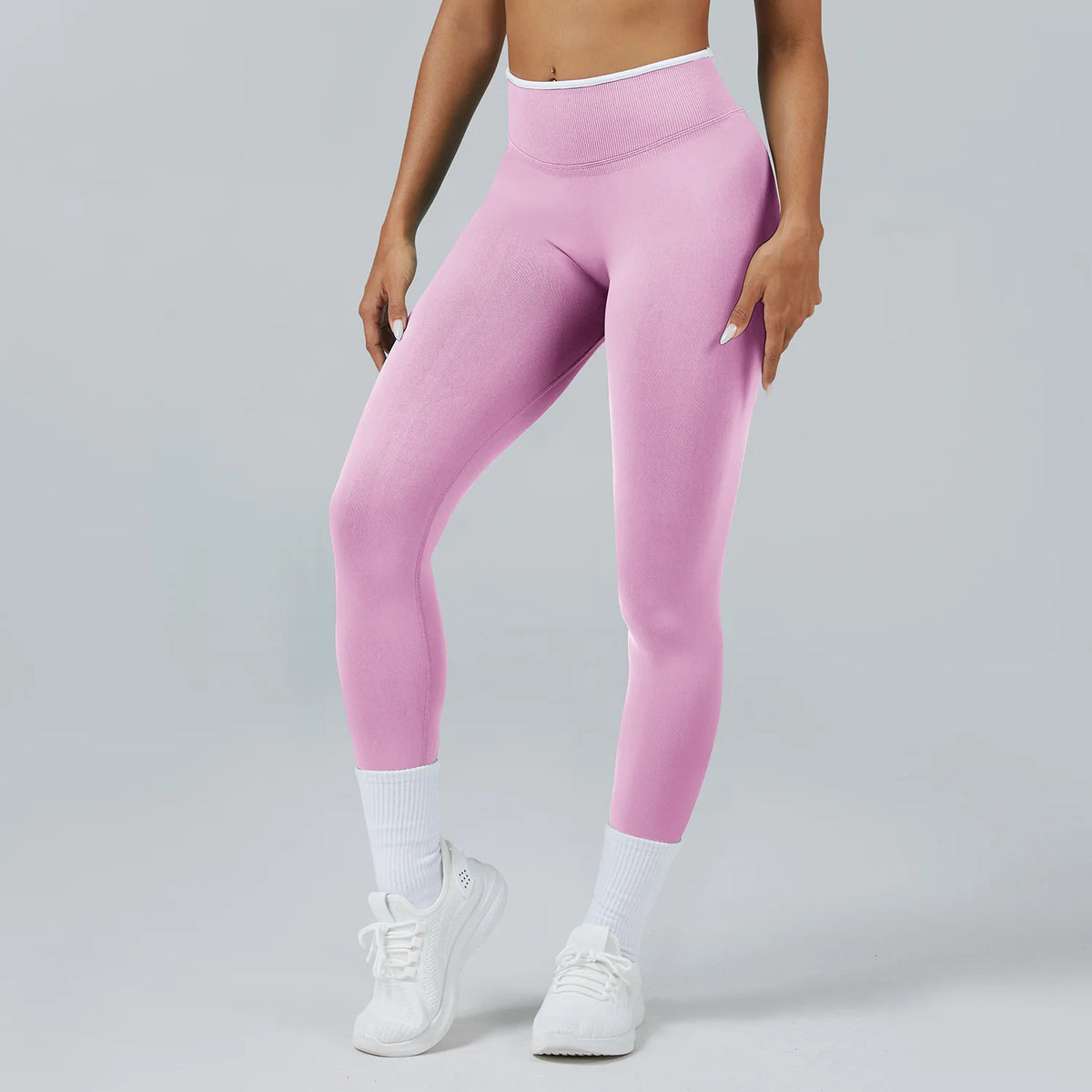 A person wearing pink high-waist yoga leggings with white socks and white sneakers.