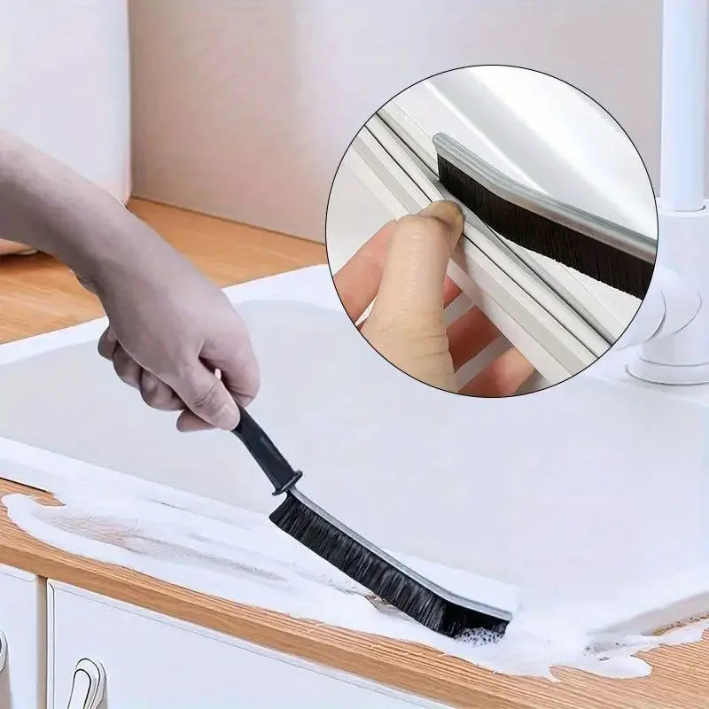 Eine Hand benutzt eine schwarze hartfasrige Spaltbürste, um Fugen und Risse auf einer weißen Oberfläche zu reinigen.