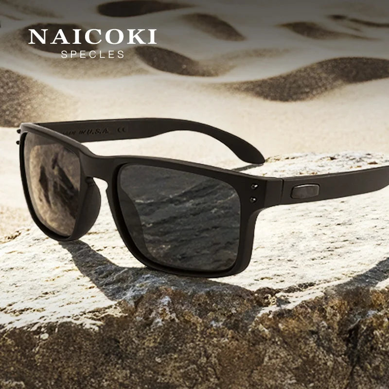 A pair of black NAICOKI spectacles resting on a rough, light-colored rock against a blurred, sandy background.