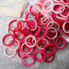 A pile of 50 pieces of mixed color elastic hair bands in pink and red are spread on a gray surface.