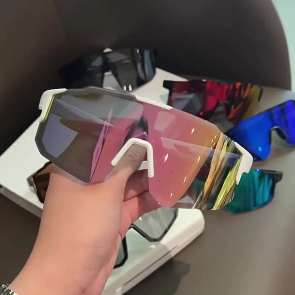 A hand holds a pair of pink and gold sport cycling and skiing goggles against a dark background.