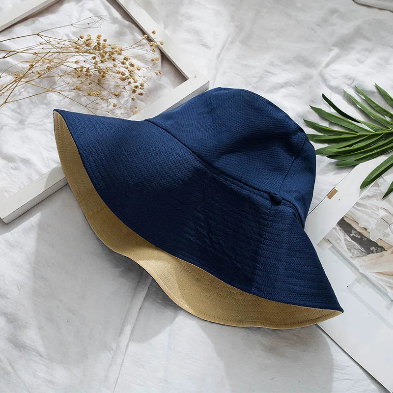 A navy blue double-sided wide brim bucket hat with a tan accent resting on a white surface.