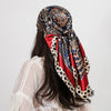A woman wearing a silk paisley shawl scarf with blue, red, and gold patterns over a white top.