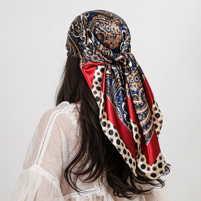 A woman wearing a silk paisley shawl scarf with blue, red, and gold patterns over a white top.