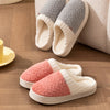 A pair of cozy plush fleece slippers in pink and cream colors resting on a wooden floor.