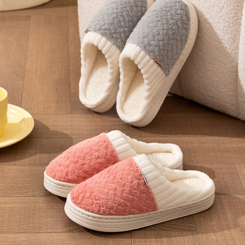 A pair of cozy plush fleece slippers in pink and cream colors resting on a wooden floor.