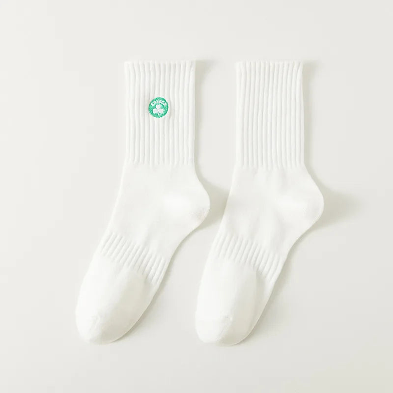 A pair of white men's athletic crew socks with a green embroidered clover design.