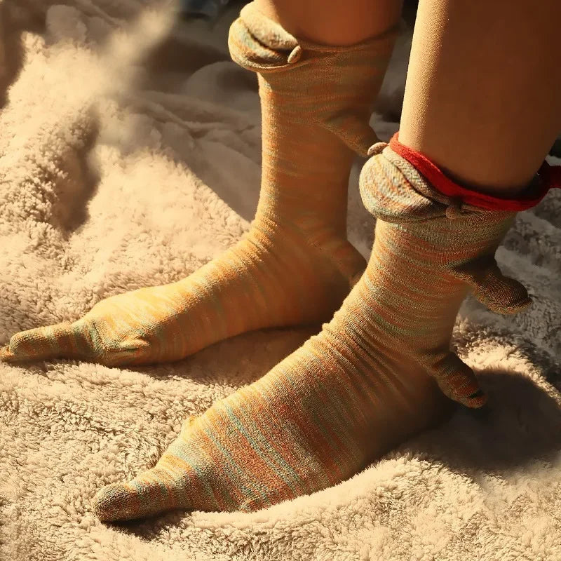 A pair of knitted crocodile-themed socks in beige and orange stripes resting on a fluffy, light-colored surface.