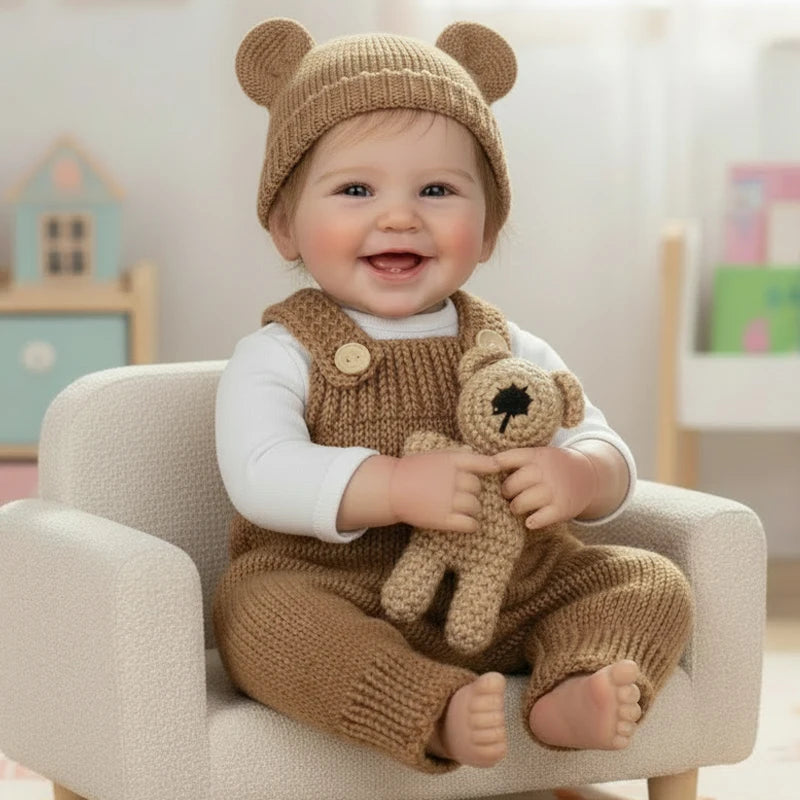 Lachendes Baby mit handgewebtem Bärenhut und passender Kleidung, sitzt auf einem hellen Stuhl.