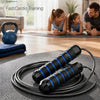 A black adjustable weighted speed jump rope is laid out on a dark mat with coiled ropes visible.