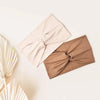 A beige and brown fabric turban headband is shown folded on a light background.