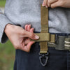 A hand is fastening a tactical nylon glove hook onto a dark belt.