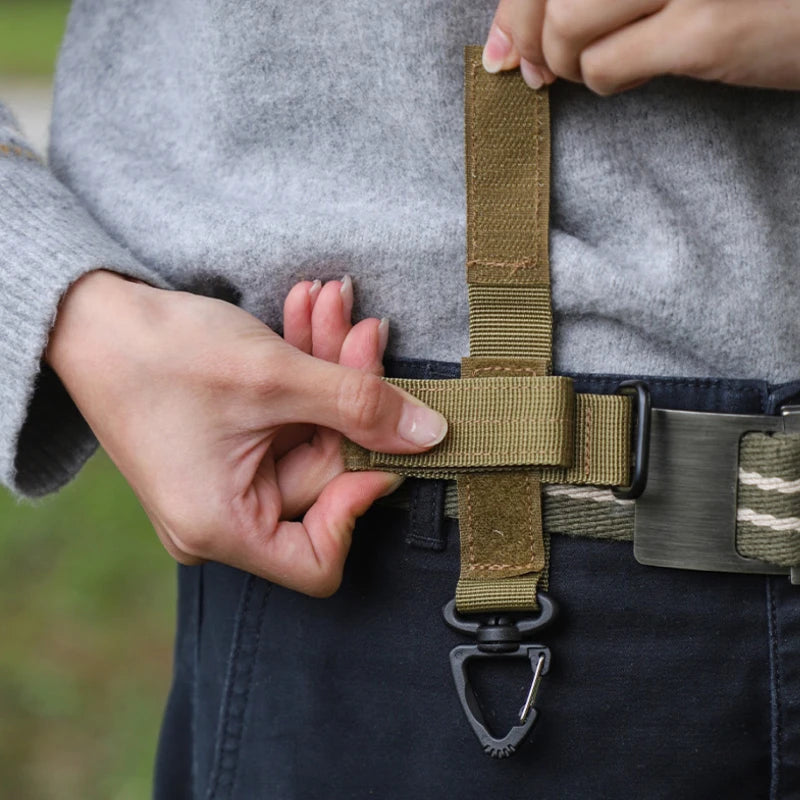 A hand is fastening a tactical nylon glove hook onto a dark belt.
