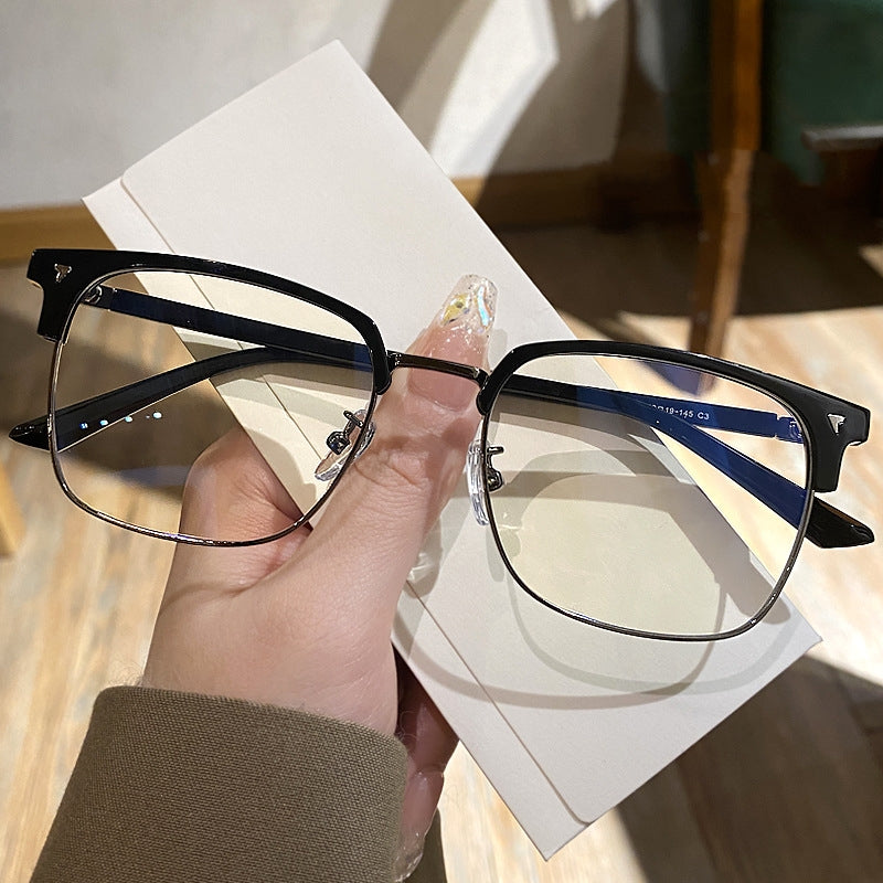 A hand holds a pair of retro square blue light blocking eyeglasses against a white background.