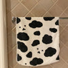 A white and black cow print face towel hanging on a metal rack against a tiled wall.