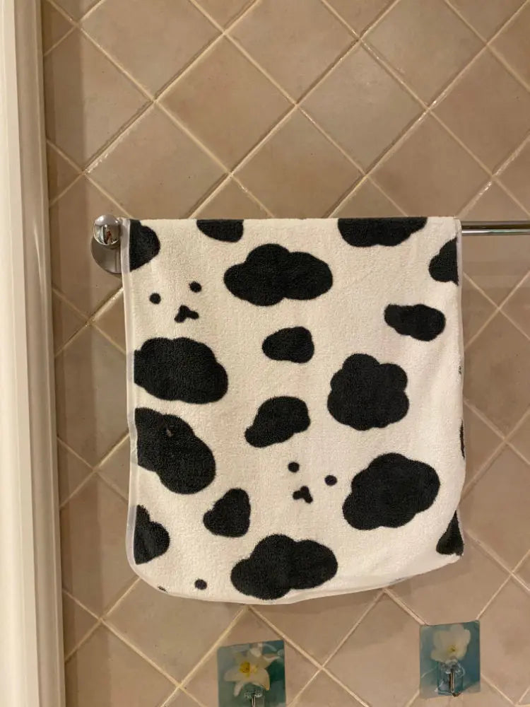 A white and black cow print face towel hanging on a metal rack against a tiled wall.